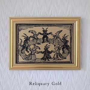 May include: A framed print with a gold-colored frame. The print depicts a circle of dancing figures with horns and pointed hats. The text "Reliquary Gold" is at the bottom.