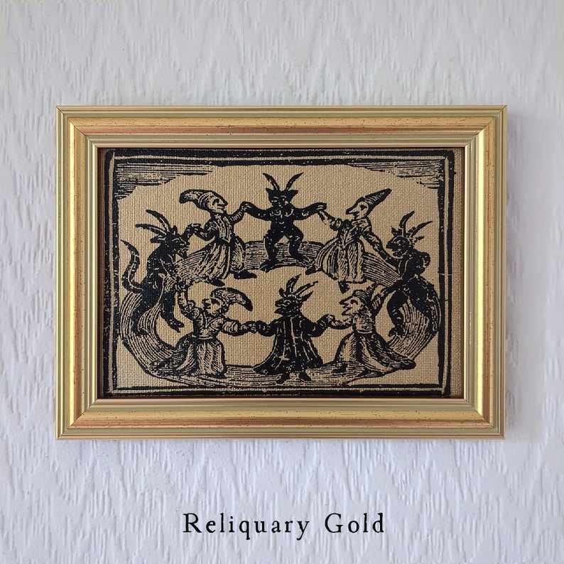 May include: A framed print with a gold-colored frame. The print depicts a circle of dancing figures with horns and pointed hats. The text "Reliquary Gold" is at the bottom.