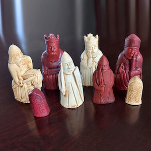 Peut inclure: Un ensemble de huit répliques de pièces d'échecs de Lewis aux couleurs crème et rouge profond. Le set comprend des rois, reines, fous, cavaliers et gardes, chacun présentant des expressions sculptées, des robes et des accessoires détaillés.