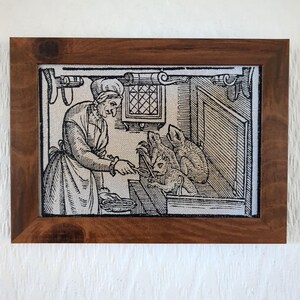 Könnte beinhalten: Ein Schwarz-Weiß-Holzschnitt, der eine Frau in einem langen Kleid zeigt, die drei Tiere aus einer Schüssel füttert. Die Frau hält einen Löffel in ihrer rechten Hand und die Tiere sind um die Schüssel versammelt. Der Druck ist in einem dunklen Holzrahmen gerahmt.