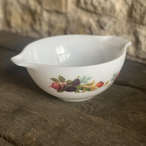 Peut inclure: Un bol mélangeur en verre opalin blanc orné d'un motif de légumes colorés sur l'extérieur. Le bol présente deux becs verseurs intégrés sur les côtés opposés et une surface intérieure lisse et arrondie pour mélanger les ingrédients.