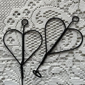 May include: Two black metal heart-shaped plant hangers with a twisted wire design.