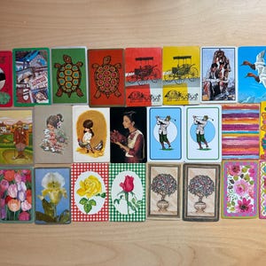 May include: A collection of vintage playing cards featuring various illustrations. The cards display images of turtles, flowers, people, and other designs. The color palette includes red, green, yellow, and blue.