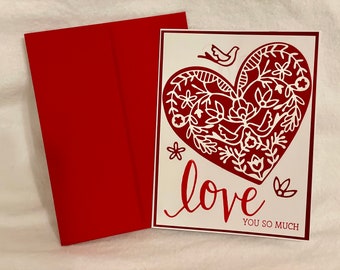 Puede incluir: Una tarjeta blanca con un diseño de corazón rojo y las palabras "love you so much". El corazón está lleno de diseños florales y de pájaros blancos.