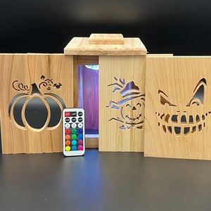 May include: Wooden Halloween lantern with interchangeable panels featuring a pumpkin, scarecrow, and jack-o'-lantern face. Includes a remote control for color-changing LED lights. The lantern is made of light-colored wood.