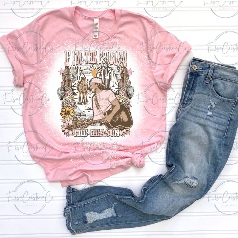 K&ouml;nnte beinhalten: Rosa T-Shirt mit einem gebleichten Design, das einen Mann zeigt, der Gitarre spielt, mit dem Text "Wenn ich das Problem bin, bist du vielleicht der Grund".