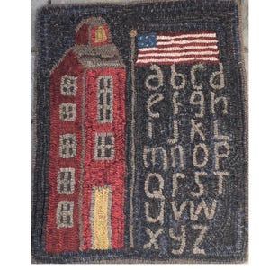 May include: A rectangular hooked rug featuring a red schoolhouse building on the left and a United States flag flying above the lowercase alphabet in tan letters on a dark background. The text Schoolhouse Sampler 23x29 is printed below the rug.