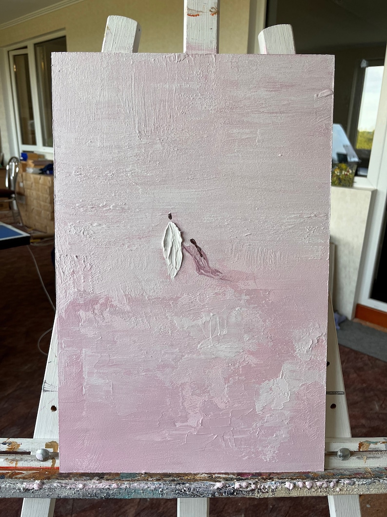 Pode incluir: Pintura abstrata em tela com fundo rosa texturizado. Uma forma branca em forma de pena e uma mancha de tinta roxa s&atilde;o aplicadas. A obra de arte &eacute; exibida em um cavalete branco.