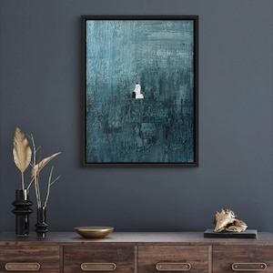 May include: A framed rectangular wall art piece featuring a deep teal and blue textured background with thick, visible brushstrokes. In the center, a small, solitary white figure is depicted in a kneeling position against the dark, moody backdrop.