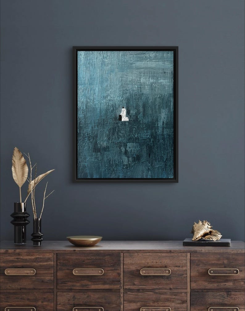 May include: A framed rectangular wall art piece featuring a deep teal and blue textured background with thick, visible brushstrokes. In the center, a small, solitary white figure is depicted in a kneeling position against the dark, moody backdrop.