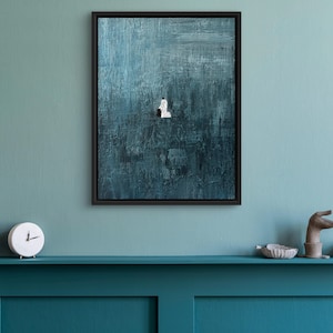 May include: A framed rectangular wall art piece featuring a deep teal and dark blue textured background with visible brushstrokes. In the center, a small, solitary white figure stands against the vast, dark, and moody painted surface.