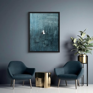 May include: A rectangular wall art piece featuring a dark teal and blue textured background with a small, centered white figure. The artwork is enclosed in a thin black frame, showcasing visible brushstrokes and a deep, moody color palette.