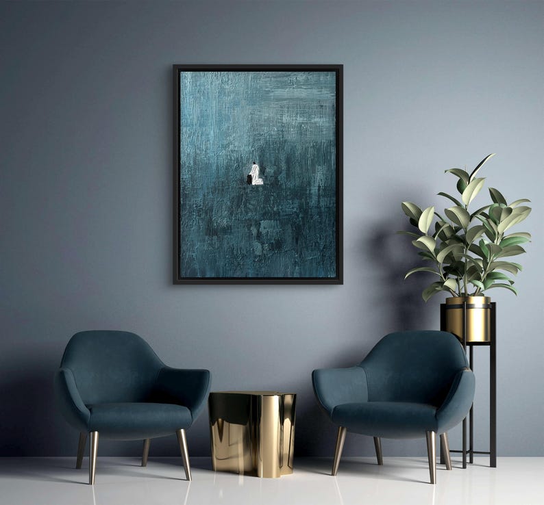 May include: A rectangular wall art piece featuring a dark teal and blue textured background with a small, centered white figure. The artwork is enclosed in a thin black frame, showcasing visible brushstrokes and a deep, moody color palette.