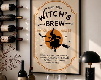 以下が含まれることがあります： 「Witch's Brew」、「Since 1692」、「Potion No. 666」という文字と、オレンジ色の月を背景に箒に乗った魔女のシルエットが描かれた額入りウォールプリント。黒いワインラック、ワインボトル2本、グラス2個、ランプと一緒に飾られています。