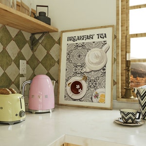 Puede incluir: Una impresi&oacute;n enmarcada con el texto "Breakfast Tea" en una fuente en blanco y negro. La impresi&oacute;n presenta una tetera blanca, una taza de t&eacute; blanca con un platillo y un plato blanco con limones sobre un fondo estampado en blanco y negro.