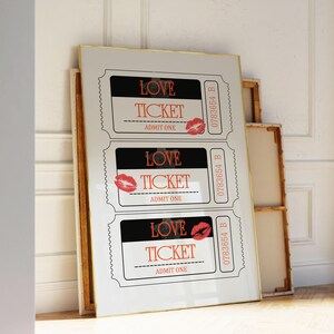 May include: Three white tickets with black borders and red lips printed on them. Each ticket says "LOVE TICKET" and "ADMIT ONE". The tickets are framed in a gold frame.