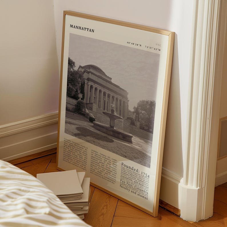 May include: A framed monochrome print of a building with columns and a fountain, labelled "Manhattan" at the top. The frame is light brown. Text at the bottom includes "Founded: 1754" and "Fun Fact: Columbia faculty and alumni."