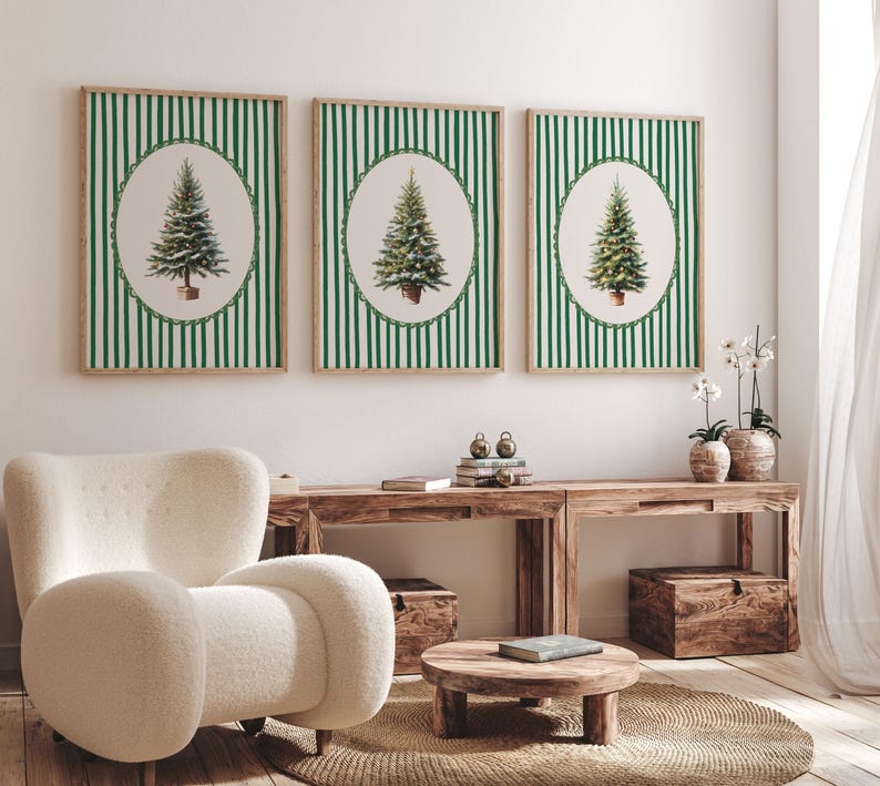 May include: Three framed prints featuring Christmas trees in oval frames against a green and white striped background. The frames are a natural wood color. The prints are displayed above a wooden console table with a white chair in the foreground.