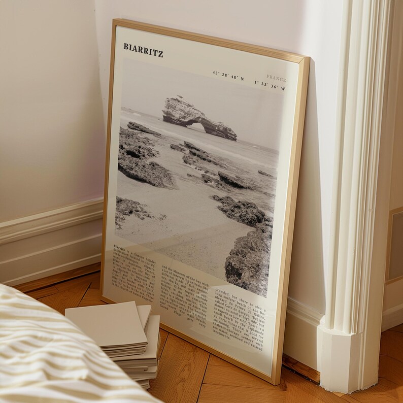 Pu&ograve; includere: Una fotografia in bianco e nero incorniciata di Biarritz, Francia, con un paesaggio costiero con una formazione rocciosa nel mare. La stampa include il nome della citt&agrave; e le coordinate. La cornice &egrave; di colore legno chiaro.
