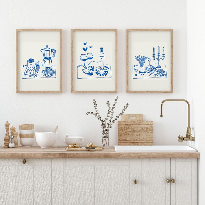 May include: Three framed illustrations of blue line drawings of food and drink on a white background. The first illustration shows a coffee pot, cups, and pastries. The second illustration shows two wine glasses, a bottle of wine, and a plate of food. The third illustration shows a plate of food, a wine glass, and a candelabra.