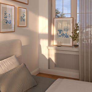 May include: A bedroom with a white bed, a white headboard, and two pillows. There are three framed pictures on the wall above the bed. A window with white curtains is on the right side of the image. The windowsill has a framed picture and a candle.