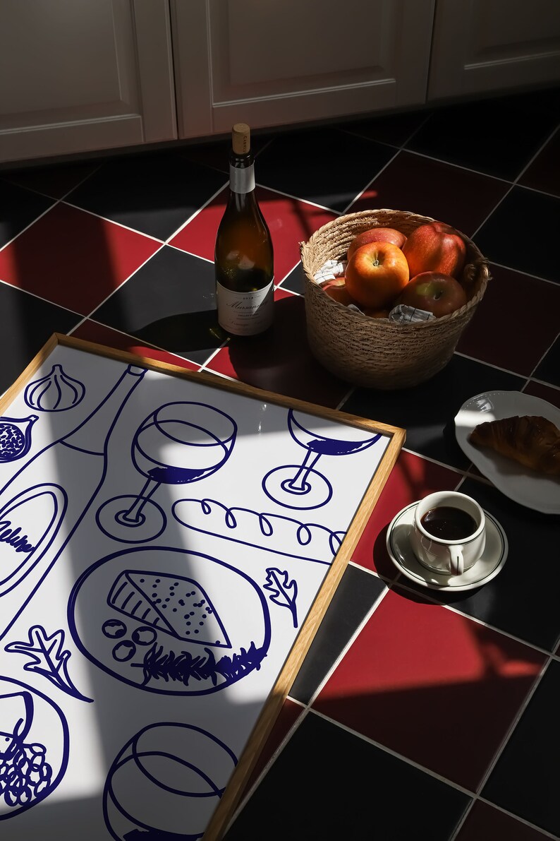 May include: A framed white drawing of a cheese plate with wine glasses, a baguette, and grapes. The drawing is on a table with a bottle of wine, a bowl of apples, and a cup of coffee.