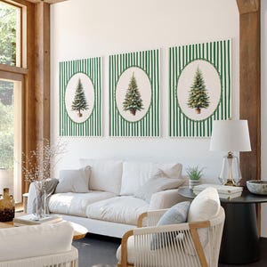 May include: Three framed Christmas tree prints. Each print features a detailed illustration of a Christmas tree in an oval frame, set against a green and white striped background. The room also includes a white sofa, chairs, and a lamp.