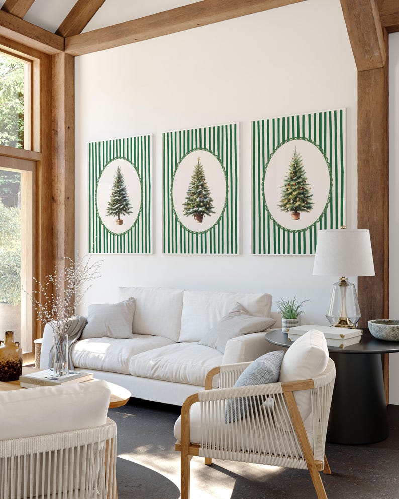 May include: Three framed Christmas tree prints. Each print features a detailed illustration of a Christmas tree in an oval frame, set against a green and white striped background. The room also includes a white sofa, chairs, and a lamp.