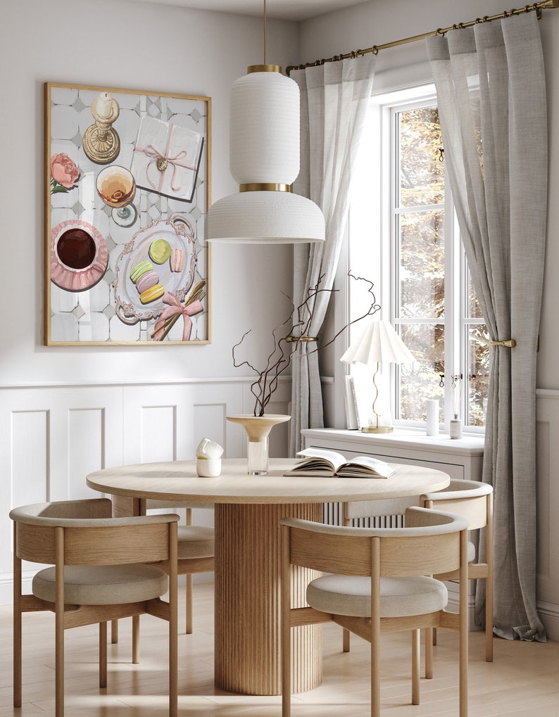 May include: A round wooden dining table with four chairs, a white pendant light, and a framed print of a still life with coffee, pastries, and a gift box. The table is set with a book and a vase with dried branches.