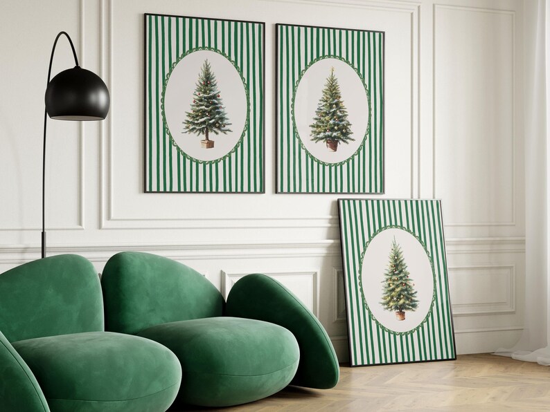 May include: Three framed Christmas tree art prints. The prints feature a green and white striped background with an oval-shaped image of a Christmas tree. The frames are black. A green velvet sofa is in the foreground.
