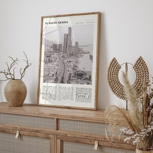 K&ouml;nnte beinhalten: Ein gerahmter Schwarz-Wei&szlig;-Druck mit dem Titel "F1 Saudi Arabia", der eine Stadtlandschaft mit Wolkenkratzern und einer K&uuml;stenstra&szlig;e zeigt. Der Druck enth&auml;lt Renndetails: Gesamtrunden: 50, Kurven: 27. Der Rahmen ist hellbraun.