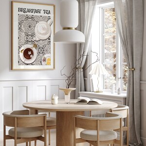 Puede incluir: Una mesa de comedor redonda de madera con cuatro sillas, un jarr&oacute;n con ramas y un libro sobre la mesa. Una l&aacute;mpara colgante blanca cuelga sobre la mesa. Una impresi&oacute;n enmarcada con el texto "Breakfast Tea" cuelga en la pared detr&aacute;s de la mesa. La impresi&oacute;n presenta una ilustraci&oacute;n estilizada de tazas de t&eacute; y una tetera sobre un fondo estampado.