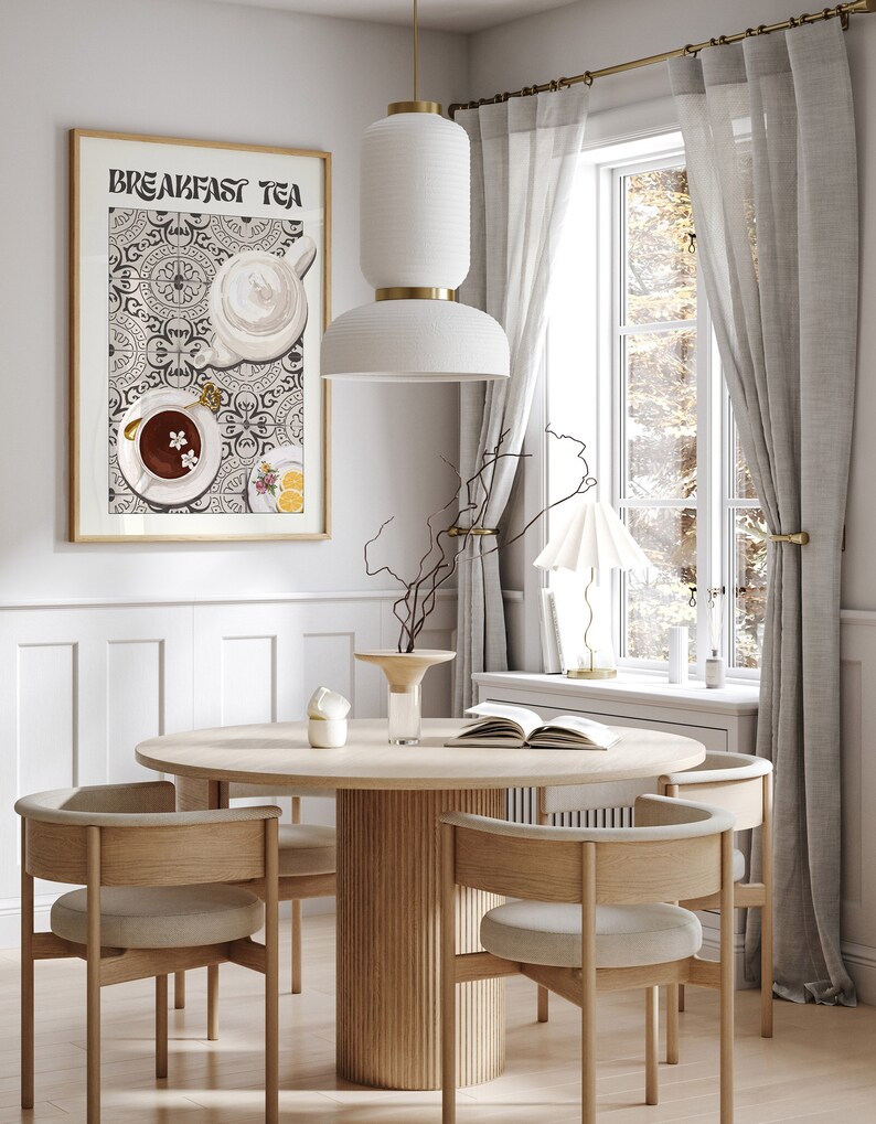 Puede incluir: Una mesa de comedor redonda de madera con cuatro sillas, un jarr&oacute;n con ramas y un libro sobre la mesa. Una l&aacute;mpara colgante blanca cuelga sobre la mesa. Una impresi&oacute;n enmarcada con el texto "Breakfast Tea" cuelga en la pared detr&aacute;s de la mesa. La impresi&oacute;n presenta una ilustraci&oacute;n estilizada de tazas de t&eacute; y una tetera sobre un fondo estampado.