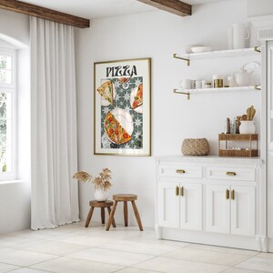 May include: A framed print of a pizza with the word "Pizza" in a stylized font. The print is hanging on a white wall in a kitchen setting. The kitchen features white cabinets, a white countertop, and gold shelves.