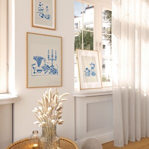 May include: Three framed illustrations of blue and white line drawings of tables with food and drinks. The illustrations are hanging on a white wall in a room with a window and white curtains.