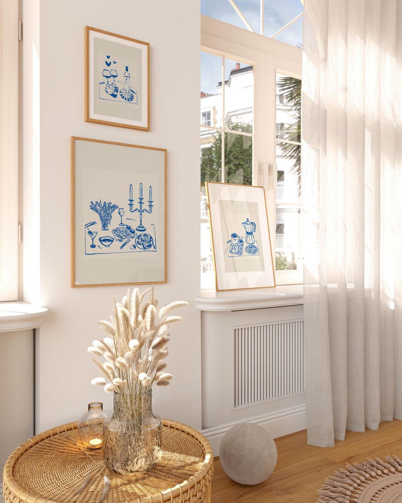 May include: Three framed illustrations of blue and white line drawings of tables with food and drinks. The illustrations are hanging on a white wall in a room with a window and white curtains.