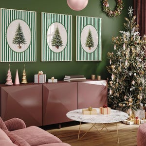 May include: Three framed Christmas tree prints with green and white striped backgrounds hang above a burgundy cabinet. A decorated Christmas tree stands to the right, with a marble coffee table in front.