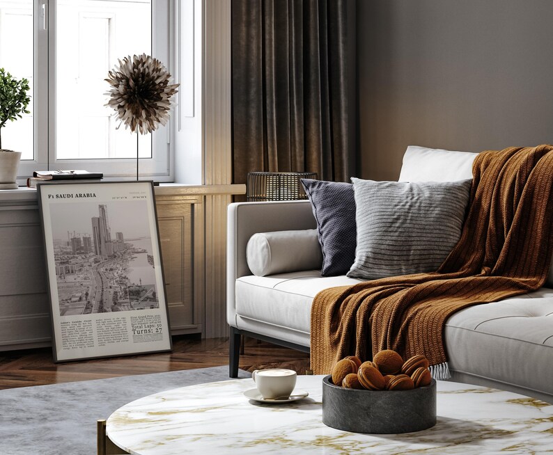 K&ouml;nnte beinhalten: Ein Wohnzimmer mit einem wei&szlig;en Sofa, Kissen und einer rostfarbenen Decke. Ein Marmor-Couchtisch zeigt eine Schale mit Keksen und eine Kaffeetasse. Ein gerahmter Druck mit Text ist in der N&auml;he eines Fensters zu sehen.