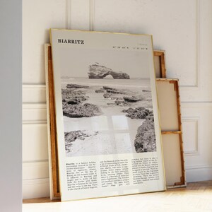 Pu&ograve; includere: Una fotografia in bianco e nero incorniciata di Biarritz, Francia, appoggiata a un muro. La fotografia presenta una scena costiera con una formazione rocciosa nell'oceano. La cornice ha un bordo dorato. Il testo in alto recita "BIARRITZ".