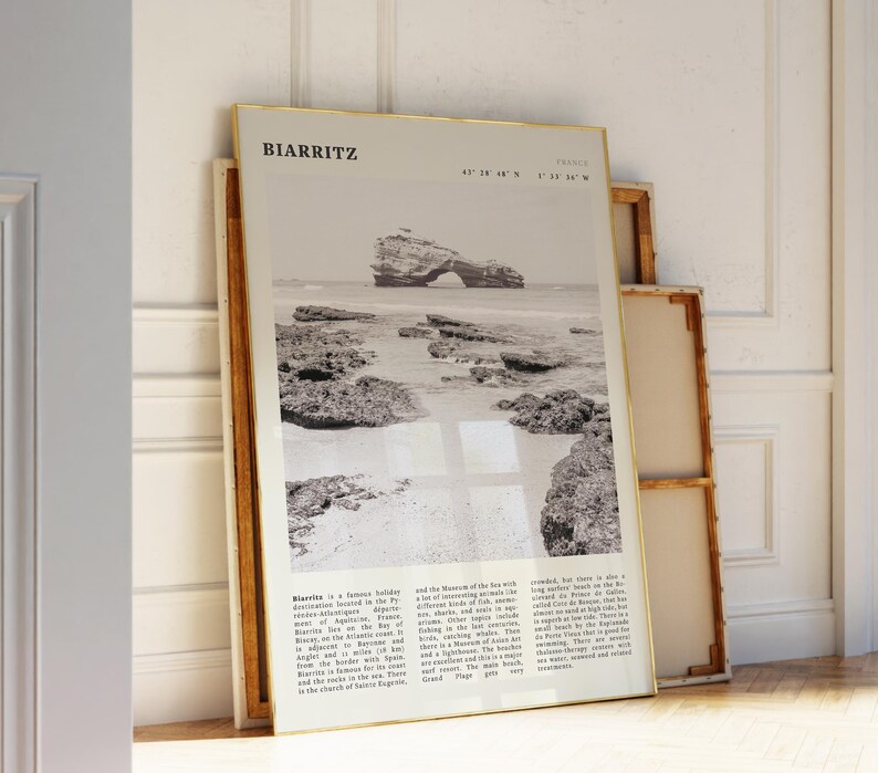 Pu&ograve; includere: Una fotografia in bianco e nero incorniciata di Biarritz, Francia, appoggiata a un muro. La fotografia presenta una scena costiera con una formazione rocciosa nell'oceano. La cornice ha un bordo dorato. Il testo in alto recita "BIARRITZ".
