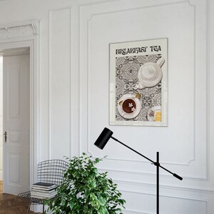 Puede incluir: Una pared blanca con un p&oacute;ster en blanco y negro que dice "Breakfast Tea" y presenta una tetera blanca y una taza de t&eacute; sobre un fondo estampado. Una l&aacute;mpara de pie negra se encuentra en la esquina inferior izquierda de la imagen.
