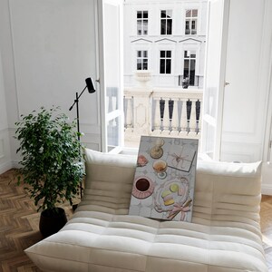 May include: A white couch with a framed print of a still life featuring a pink rose, a glass of wine, a box tied with a pink ribbon, and macarons on a plate.