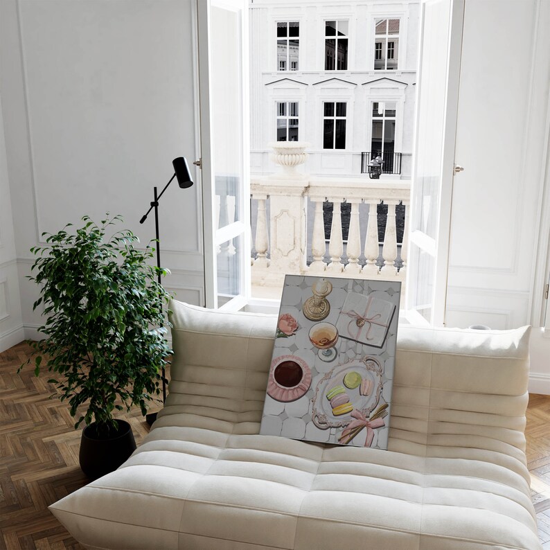 May include: A white couch with a framed print of a still life featuring a pink rose, a glass of wine, a box tied with a pink ribbon, and macarons on a plate.