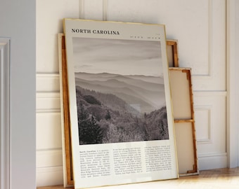 May include: A framed print titled "North Carolina" with a gold frame, leaning against a wall. The print features a black and white landscape of mountains and text describing the state's geography and attractions.