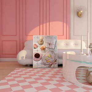 May include: A framed print of a still life featuring a glass of wine, a cup of coffee, macarons, and a gift box on a tiled surface. The print is hanging on a pink wall above a white sofa.