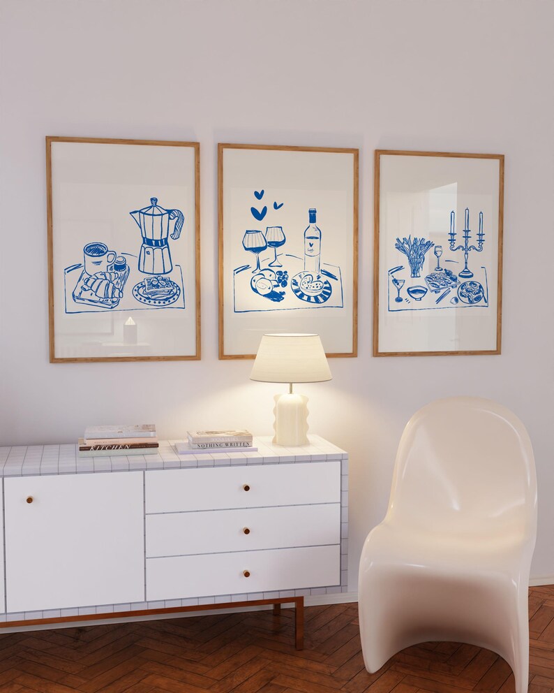 May include: Three framed illustrations of blue line drawings depicting different meals on trays. The first illustration shows a coffee pot, coffee cup, and pastries. The second illustration shows a bottle of wine, two glasses of wine, and a plate of food. The third illustration shows a plate of food, a glass of wine, and a candelabra with candles.