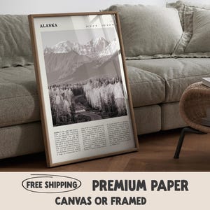 May include: A framed monochrome print depicting a mountain landscape in Alaska, with a road winding through a forest. The print is in a wooden frame and has the word "Alaska" at the top.
