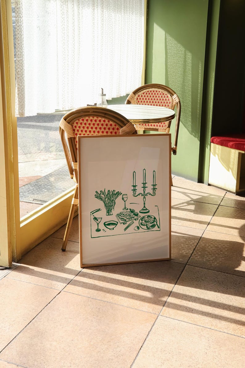 Puede incluir: Una impresi&oacute;n enmarcada de un dibujo de l&iacute;nea verde de una mesa puesta con un candelabro, vasos y comida. La impresi&oacute;n est&aacute; colgada en una pared en un ambiente de cafeter&iacute;a.