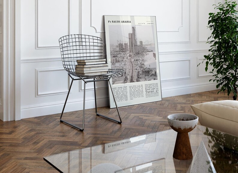 K&ouml;nnte beinhalten: Ein modernes Wohnzimmer mit einem Drahtstuhl mit B&uuml;chern, einem gerahmten Poster mit dem Text "F1 Saudi Arabia" und einer kleinen Schale auf einem Holztisch. Der Raum hat wei&szlig;e W&auml;nde und Parkettboden.