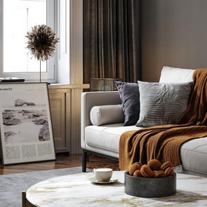 Pu&ograve; includere: Un soggiorno con un divano bianco, cuscini e una coperta color ruggine. &Egrave; visibile una stampa in bianco e nero di una scena costiera. Un tavolino con una ciotola di biscotti e una tazza di caff&egrave;.
